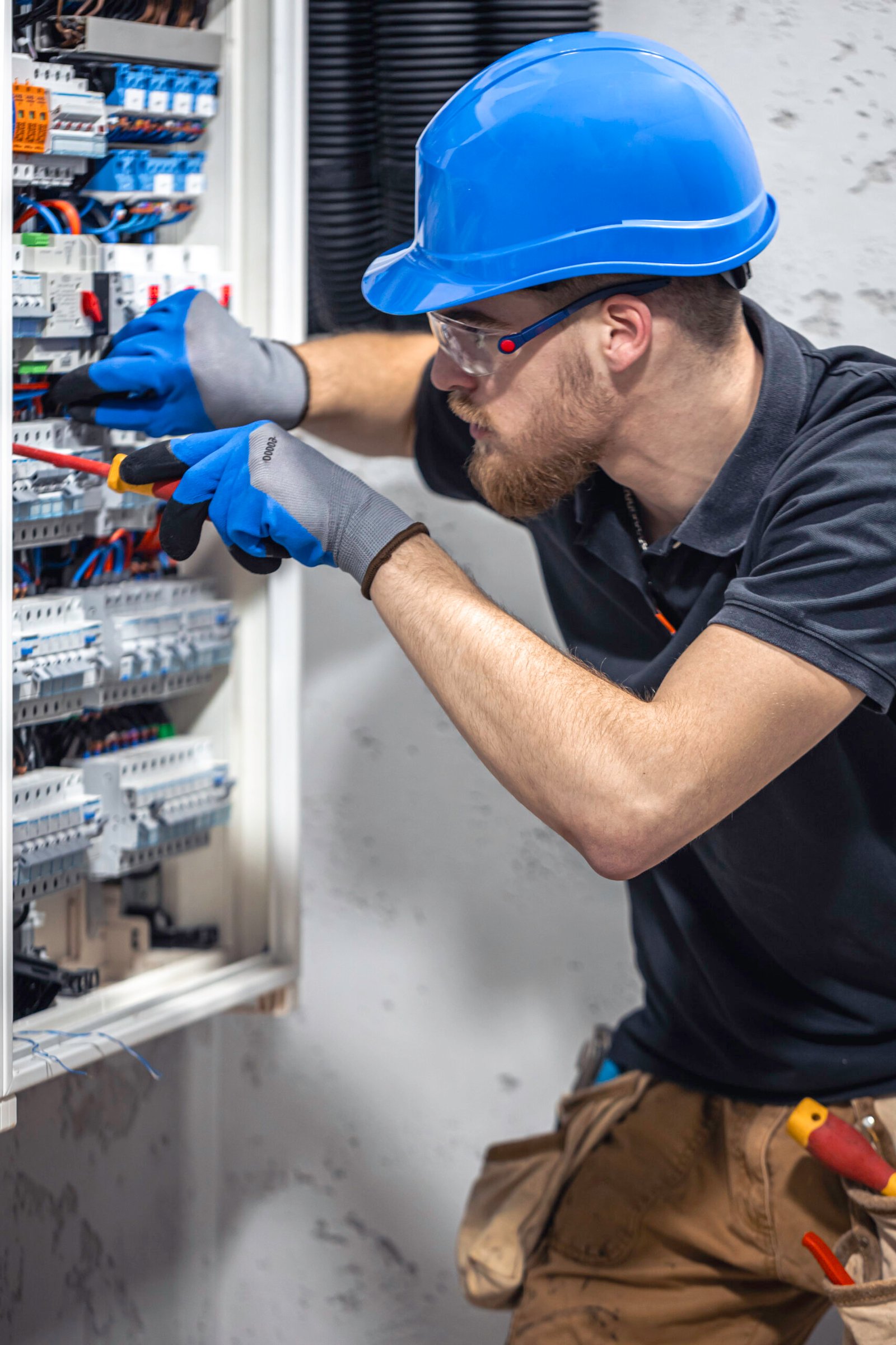 A male electrician works in a switchboard with an electrical connecting cable. Electrician with screwdriver tightens electrically operated switching equipment in fuse box.